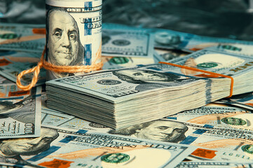 A roll of dollars with coins on the background of scattered one hundred dollar bills in blue light.