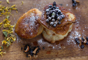 Close-up of fritters with fresh blueberries in icing sugar on a wooden table. Dried chamomile and apple.