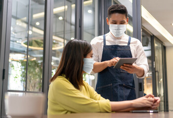 Waiter wear face mask takes order from Asian Woman with digital tablet