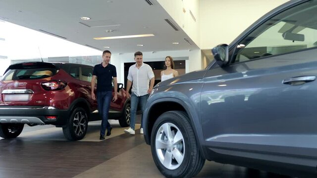 Young man choosing a new car together with dealer in auto salon