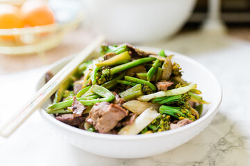 A close-up of a white bowl with Chinese beef and broccoli in a rich sauce. Horizontal photo. 
