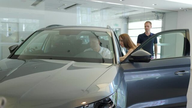 Happy couple choosing car in auto salon with a dealer