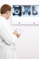 Doctor writing on clipboard while looking at X-ray images