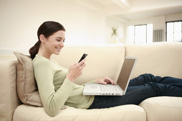 Naklejka premium Woman text messaging on the cell phone while using laptop