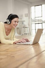 Woman with headphones lying forward on the floor using laptop