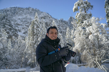 Fototapeta na wymiar Asian photographer with his professional camera posing smiling with the wonderful Yosemite landscape in winter snow as a background