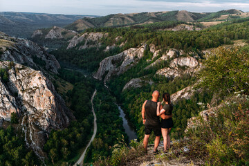 A couple meets the sunrise in the mountains, rear view. Man and woman in the mountains. Man and woman hugging. The couple travels around Russia. Travel to Russia. People greet the dawn. Copy space