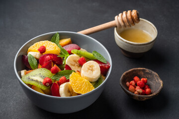 Concept of low calories delicious desserts. Summer fresh bowl with colorful fruit salad. Healthy natural organic food. Tasty sweet snack. Black background. Top view. Copy space