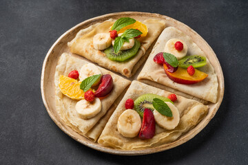 Crepes with fresh berries served with honey for breakfast over rustic table viewed from above. pancakes with fruits and honey on black background