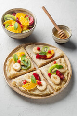 Crepes with fresh berries served with honey for breakfast over rustic table viewed from above. pancakes with fruits and honey on light background