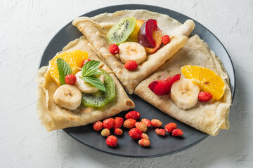 Crepes with fresh berries served with honey for breakfast over rustic table viewed from above. pancakes with fruits and honey on light background
