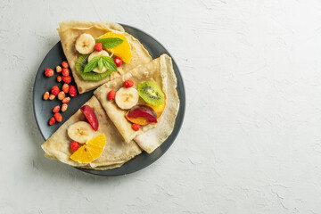 Crepes with fresh berries served with honey for breakfast over rustic table viewed from above. pancakes with fruits and honey on light background