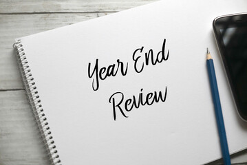 Selective focus of pencil,mobile phone and notebook written with Year End Review on white wooden...