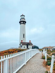 Pigeon point Lighthouse in Pescadero. White lighthouse on the Pacific coast. The tragic dark sky. Colorful flowers. Fall, summer. Free space for text. California, USA
