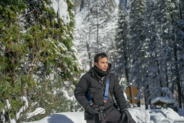 Fototapeta na wymiar Asian handsome man tourist posing at wonderful Yosemite National Park in winter surrounded by snow-covered pine trees