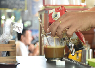 Close-up hands of barista are holding to milk box between making fresh coffee and serving to customer. 