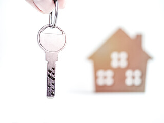 Hand holding modern metal key and miniature wooden house on white background.