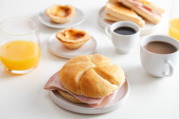 Typical Portuguese breakfast. Black coffee bica, milky coffee, bread roll with sliced cheese and ham, sandwich mixto , pastel de nata (egg tart pastry) and orange juice.