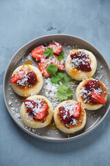 Plate with cottage cheese pancakes, fresh strawberries and coconut flakes, vertical shot over grey concrete background, selective focus