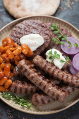 Close-up of serbian traditional grilled cevapi sausages and pljeskavicas with kajmak and prebranac, selective focus, vertical shot