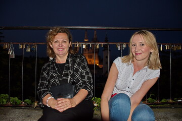 Two mature women sitting by the fence with cityscape of Zagreb against night background