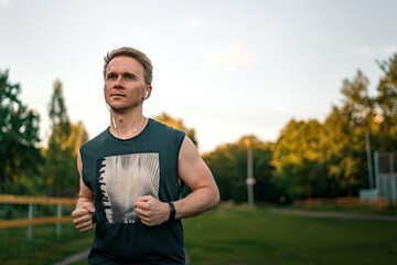 Fototapeta premium Portrait of a young man in fitness wear running in a park. Close up of a smiling man running while listening to music using earphones.