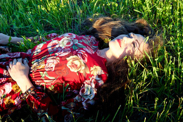 Beautiful woman or girl with magnificent figure laying on the glass in green and yellow field in the setting sun during sunset with warm yellow light. © keleny