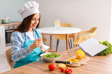 Young woman making tasty salad in kitchen