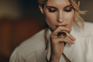 portrait of a stylish blonde woman in elegant totall beige look leather trench coat, ring, and smoky eyes makeup in the studio. Spring - autumn fashion concept. Soft selective focus.