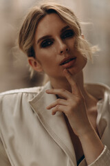 Fashionable portrait of a stylish blonde woman in elegant totall beige look leather trench coat and smoky eyes makeup in the outdoor. Spring - autumn fashion concept. Soft selective focus.