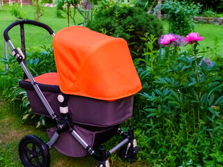 Orange baby stroller among the trees in the garden