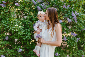 Obraz premium Young beautiful woman kisses baby girl in the cheek in summer