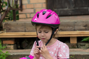 A little girl puts on a protective helmet sitting on the steps of country house