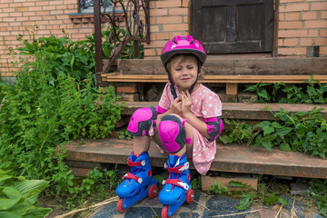 A little girl puts on a protective helmet sitting on the steps of country house