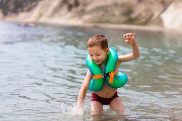 a boy in a life jacket is standing on the seashore and splashes