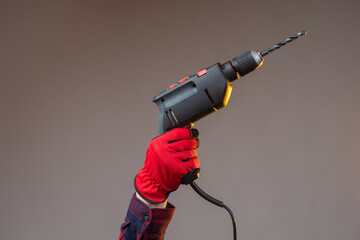 Hand with an electric drill. Construction electric tool. Hands in construction gloves. Electric drill on a dark background. Concept - drilling holes. Concept - sale of drills for construction.