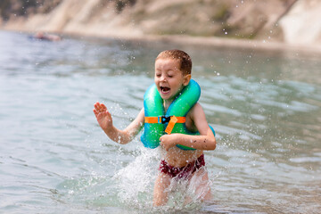 a boy in a life jacket is standing on the seashore and splashes
