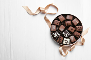 Delicious chocolate candies in box on white wooden table, flat lay. Space for text
