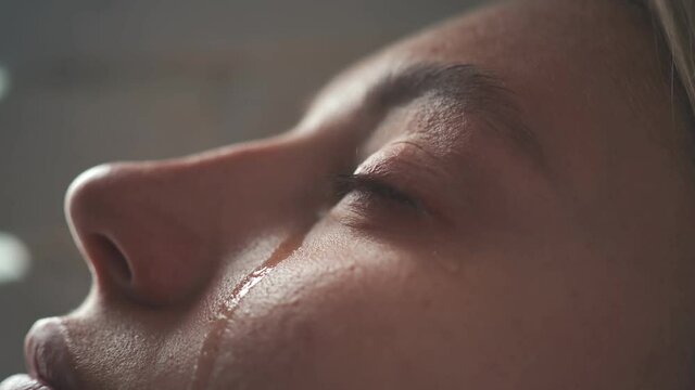 Close-up of the crying face of a young girl, from whose eyes two tears flow. The girl is lying on her back, a close-up of tears coming down the girl's cheek