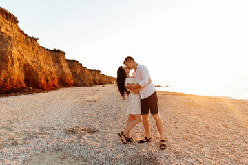 Loving couple in white clothes during a honeymoon at sea walk on the sand at a photoshoot Love Story, ocean coast, beach