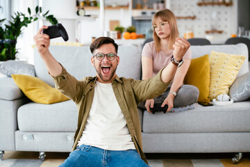 Naklejka premium Husband and wife playing video game with joysticks in living room. Loving couple are playing video games at home. 