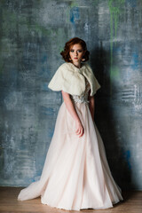 Portrait of red haired girl wearing wedding dress against a white studio background.