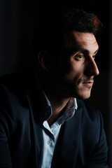 Close up portrait of a serious man 30-34 years old in a blue shirt and a dark jacket on a black background.