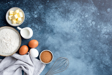 Baking ingredients flour eggs sugar milk and butter on a painted blue background. Top view copy...