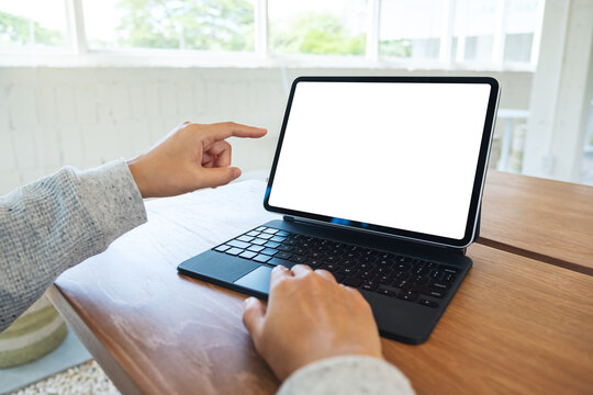 Mockup image of a woman using and pointing finger at tablet pc with blank desktop white screen as a computer pc on wooden table