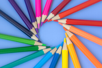 Swirl of colored pencils on a blue background. Goods for school and kindergarten. Tools for creativity and drawing. Color palette.