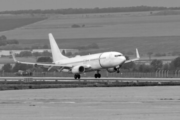 Fototapeta na wymiar Side view of white commercial passenger jet airliner in flight landing on airport runway. Black and white widescreen frame. Modern technology in fast transportation, business travel aviation, tourism.