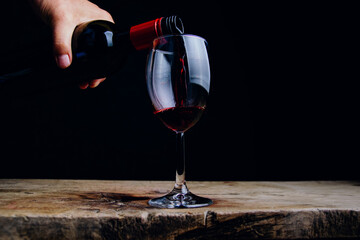 Red wine pours from a bottle into a glass on a dark background