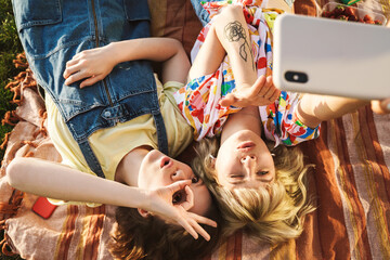 Image of two women taking selfie on cellphone and gesturing ok sign
