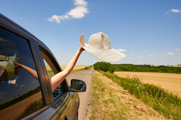 Female hand with a hat from a car window on the road.